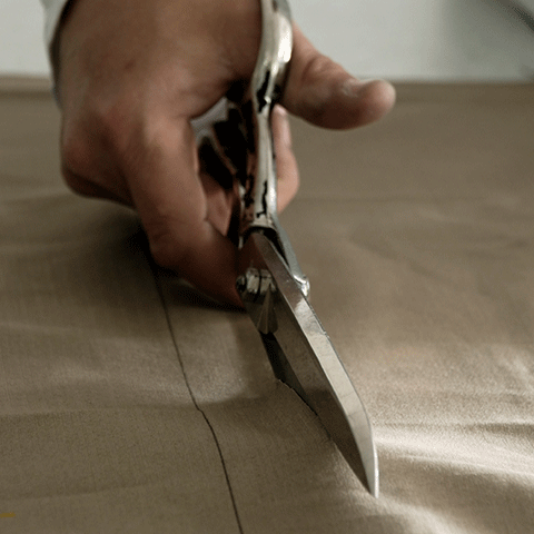 A man's hand cutting a piece of fabric with large scissors